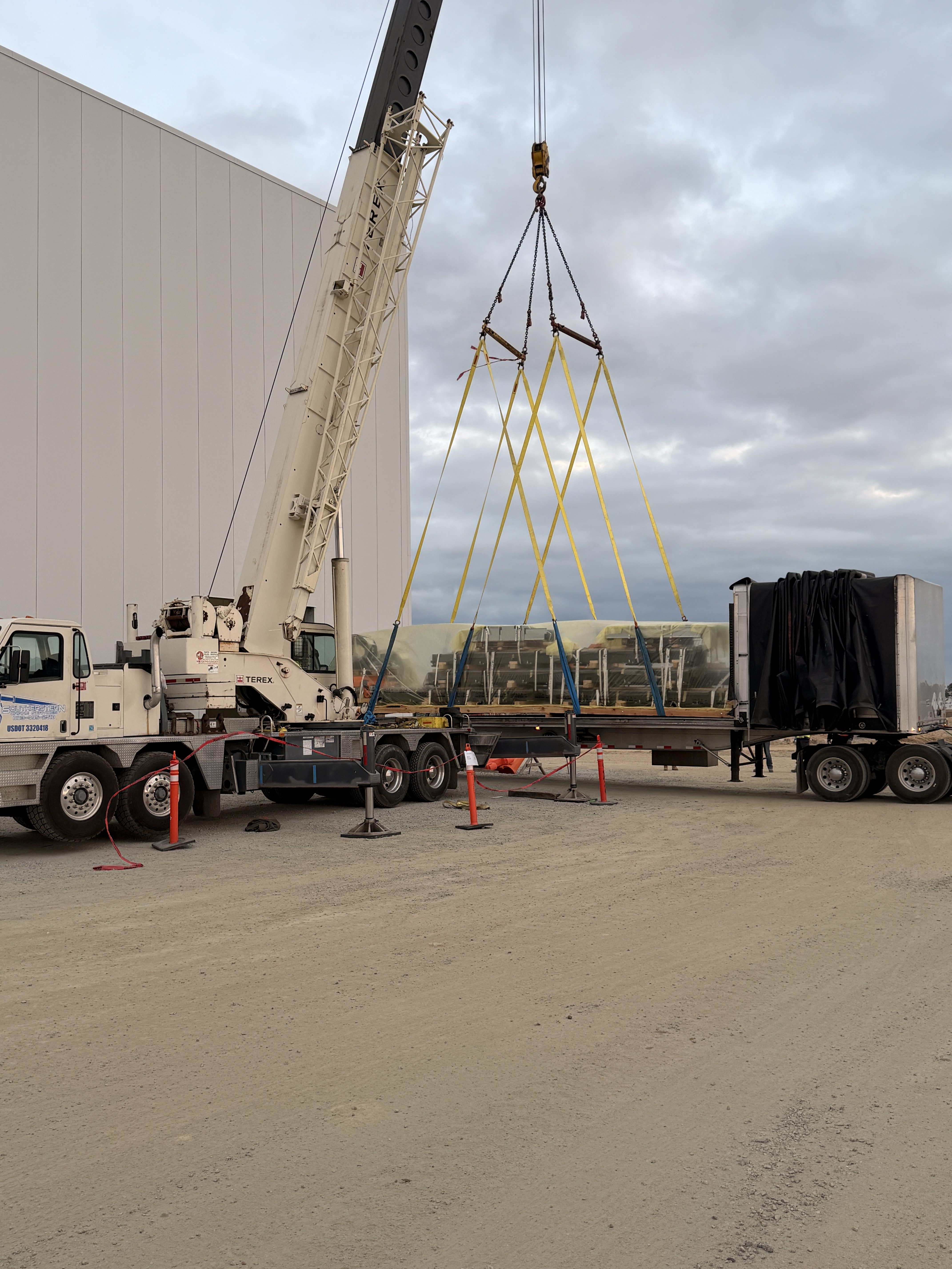 Mobile crane performing a critical lift while unloading equipment at a construction site.